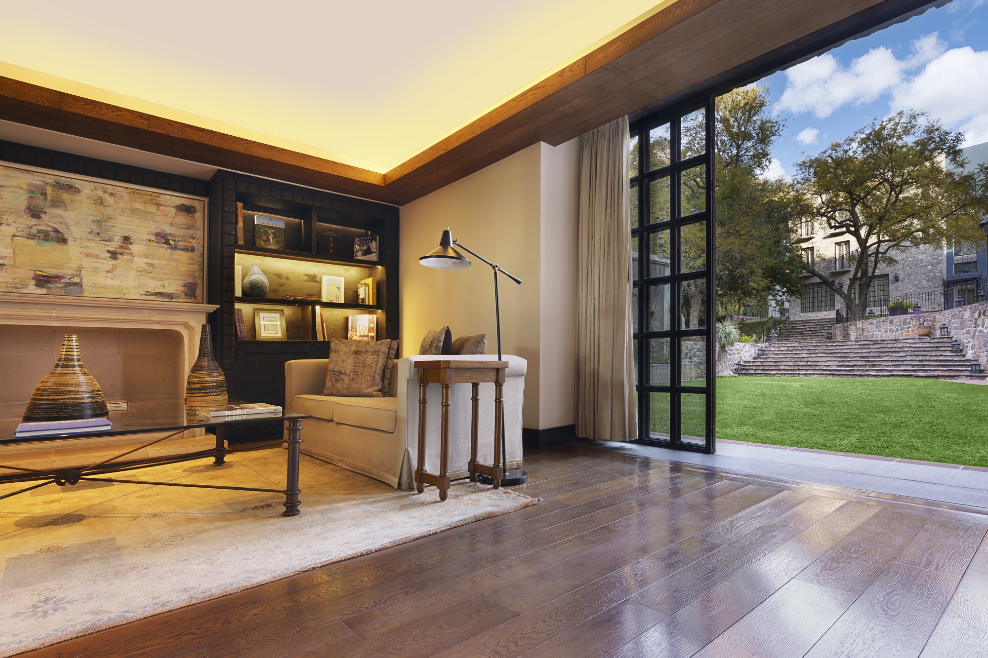 Cozy seating by bookshelf and lamp, opens to lush garden at Banyan Tree Puebla's lobby.